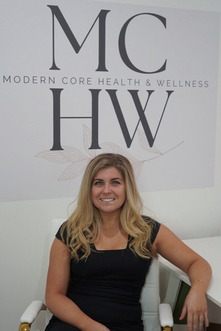 Dr. Corrine Macchi, PT, DPT, founder of Modern Core Health & Wellness, in front of the studio sign